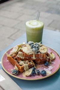 Vegane Waffel mit Obst und Mandelmus auf einem pinken Teller im Café Om Nom Nom in Sendling